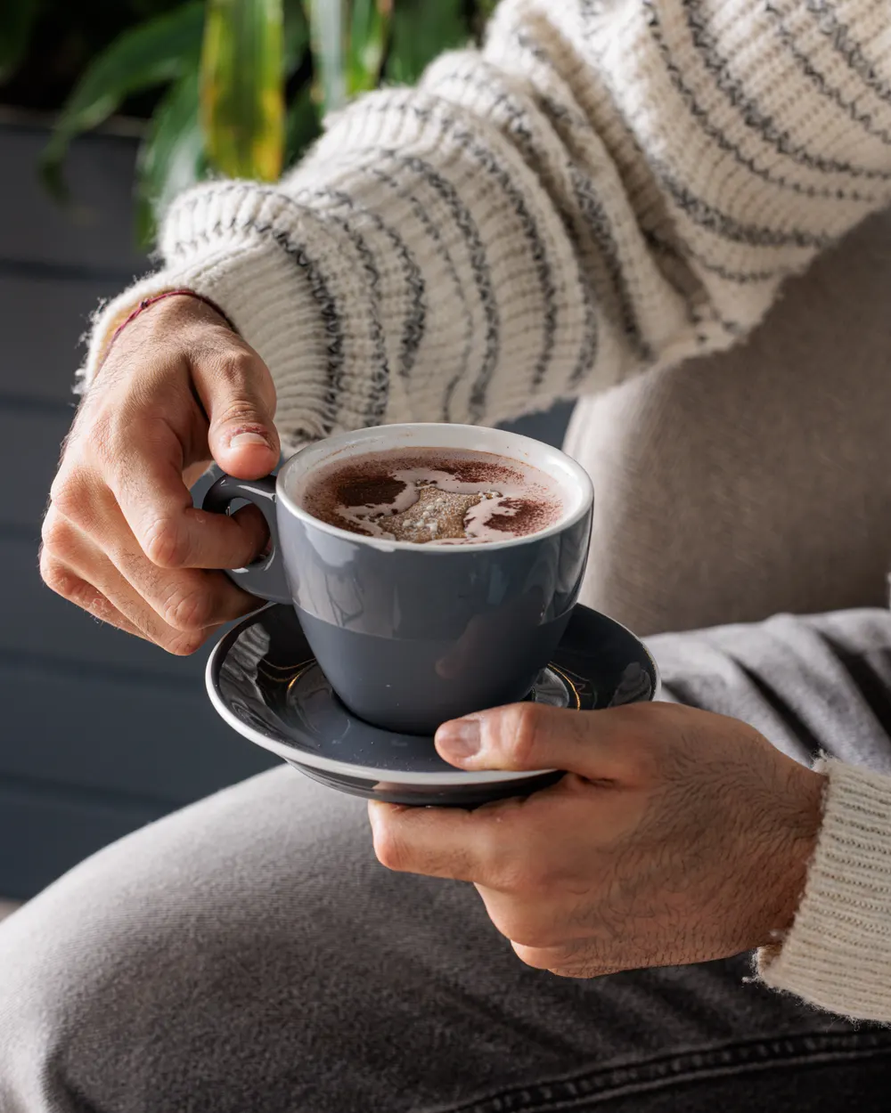 Hands holding a grey cup and saucer
